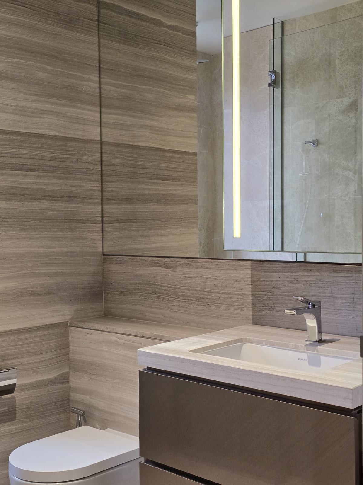 A bathroom with horizontally veined stone-look walls, a wall-hung vanity and a mirror with an integrated light strip.