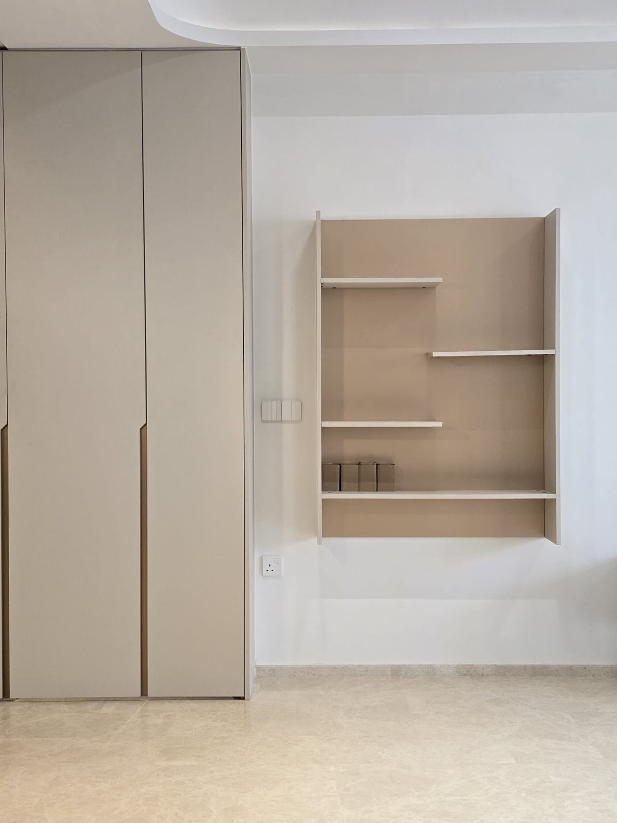 A bedroom wall of full-height pale wardrobes with recessed pulls, beside a timber-toned open shelf niche.