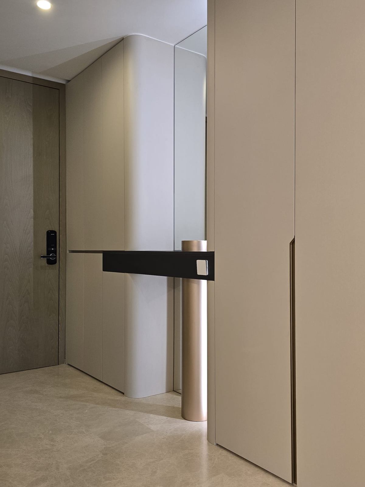 The entrance door beside a curved joinery wall, with a dark console shelf supported on a bronze-toned column.