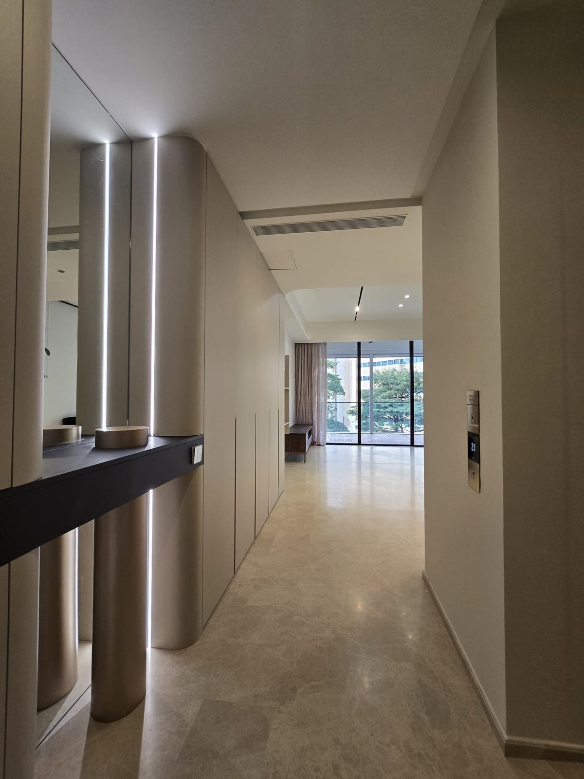 Entry gallery lined with full-height pale joinery, rounded columns with vertical light lines and a dark floating console, leading to a window and balcony.