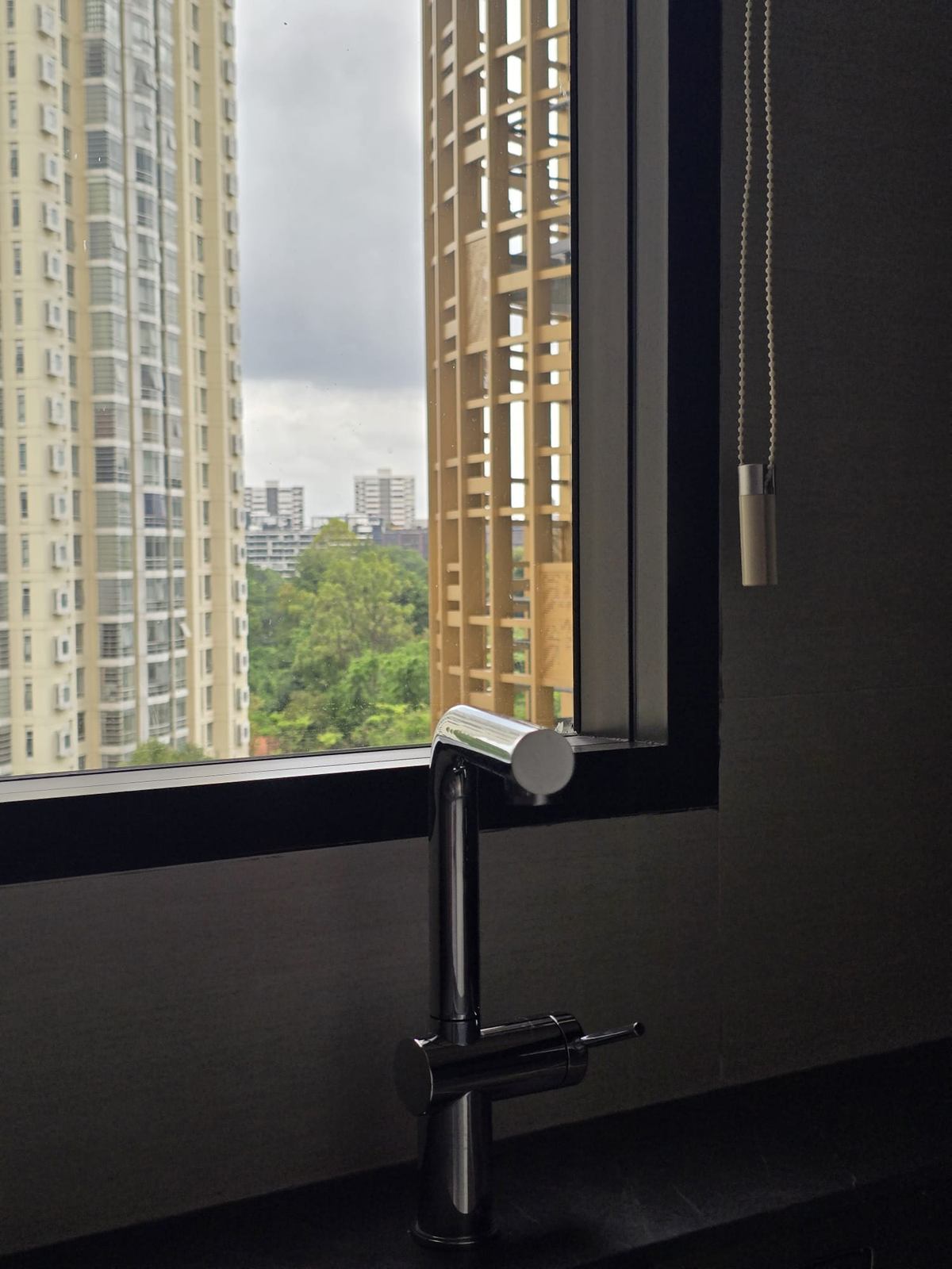 A dark kitchen tap in front of a window with a view of trees and towers, beside a timber screen.