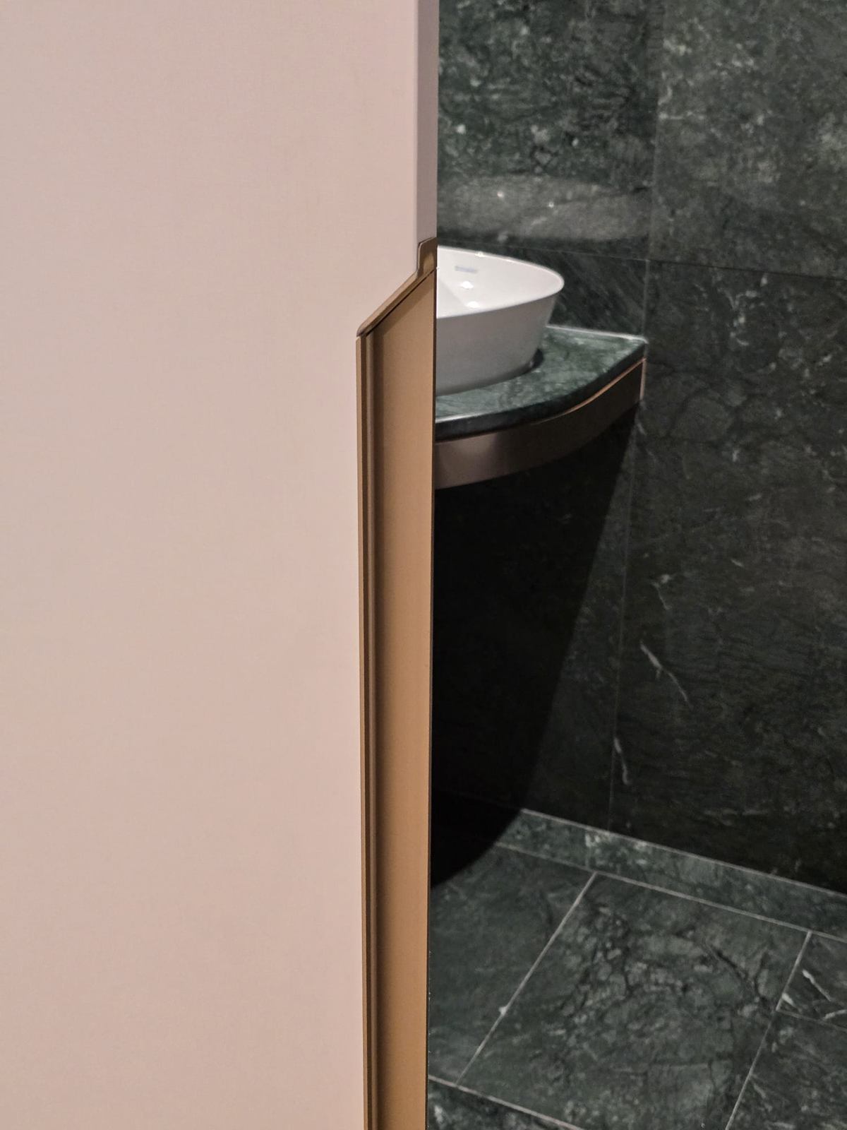 A white vessel basin on a dark green stone counter, seen past a pale wall edge.