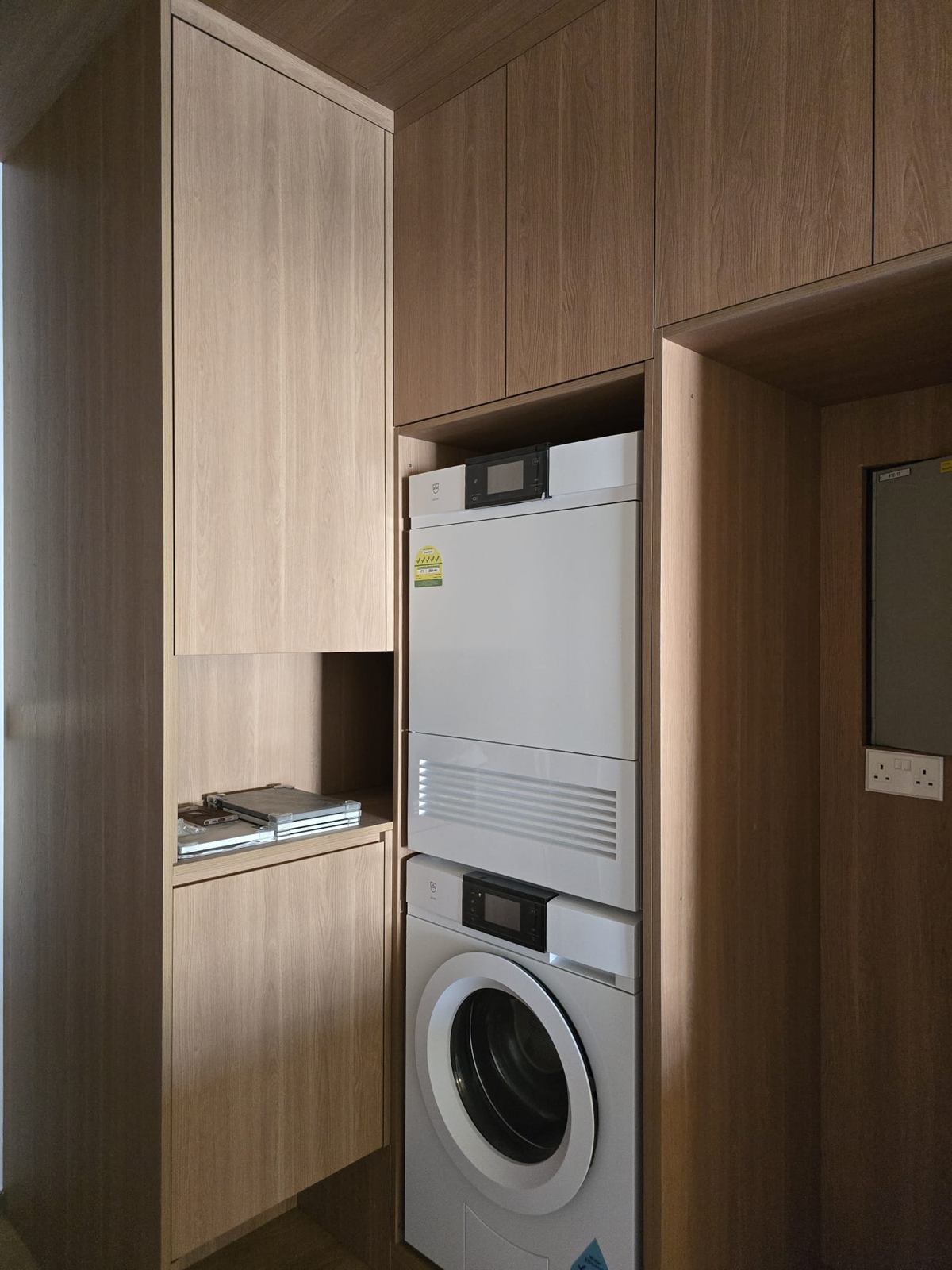 Tall timber-toned cabinets framing a stacked washer and dryer, with an open niche above.