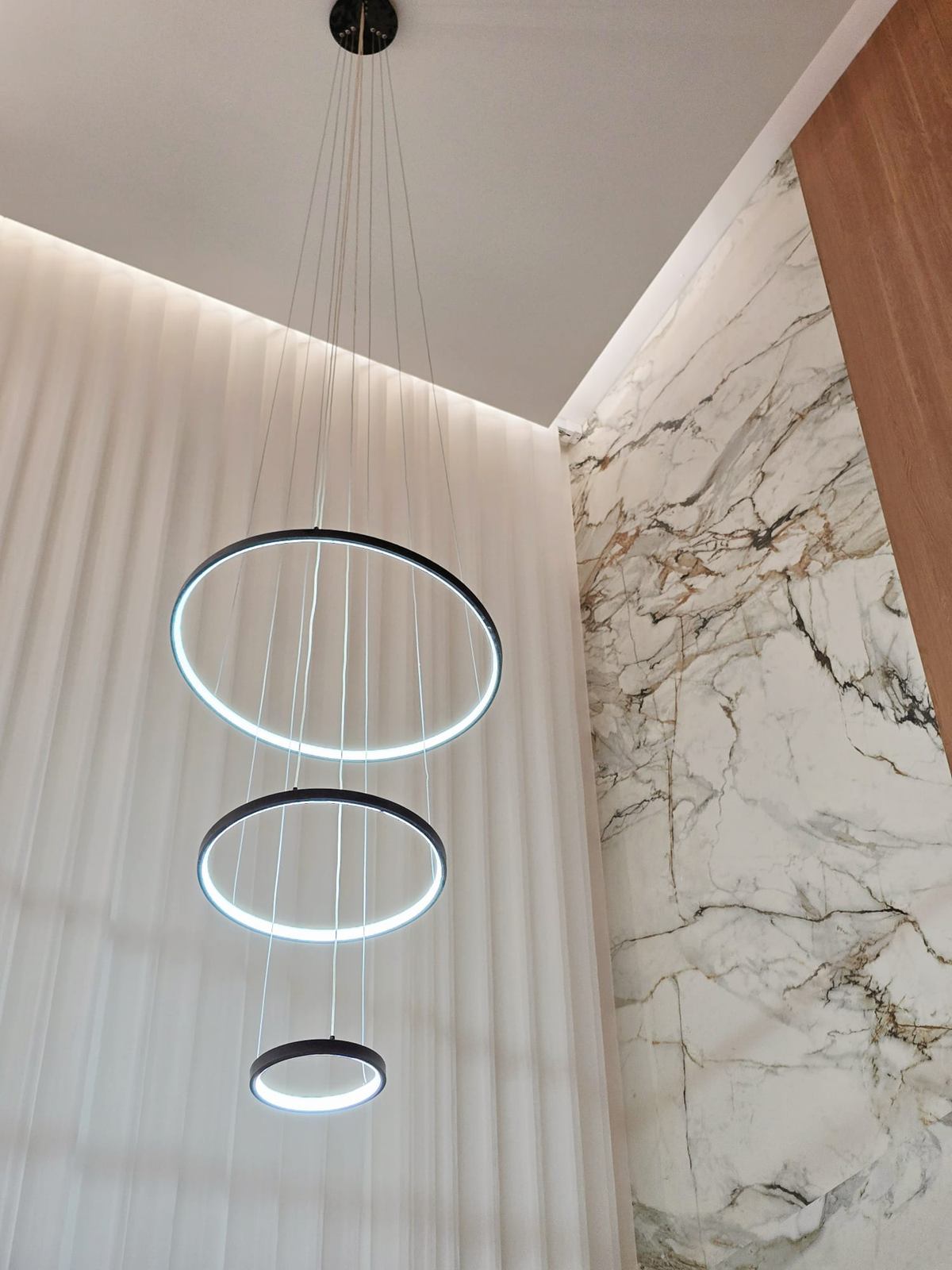 Three stacked ring pendant lights hanging beside a white marble-look feature wall with grey and gold veining.