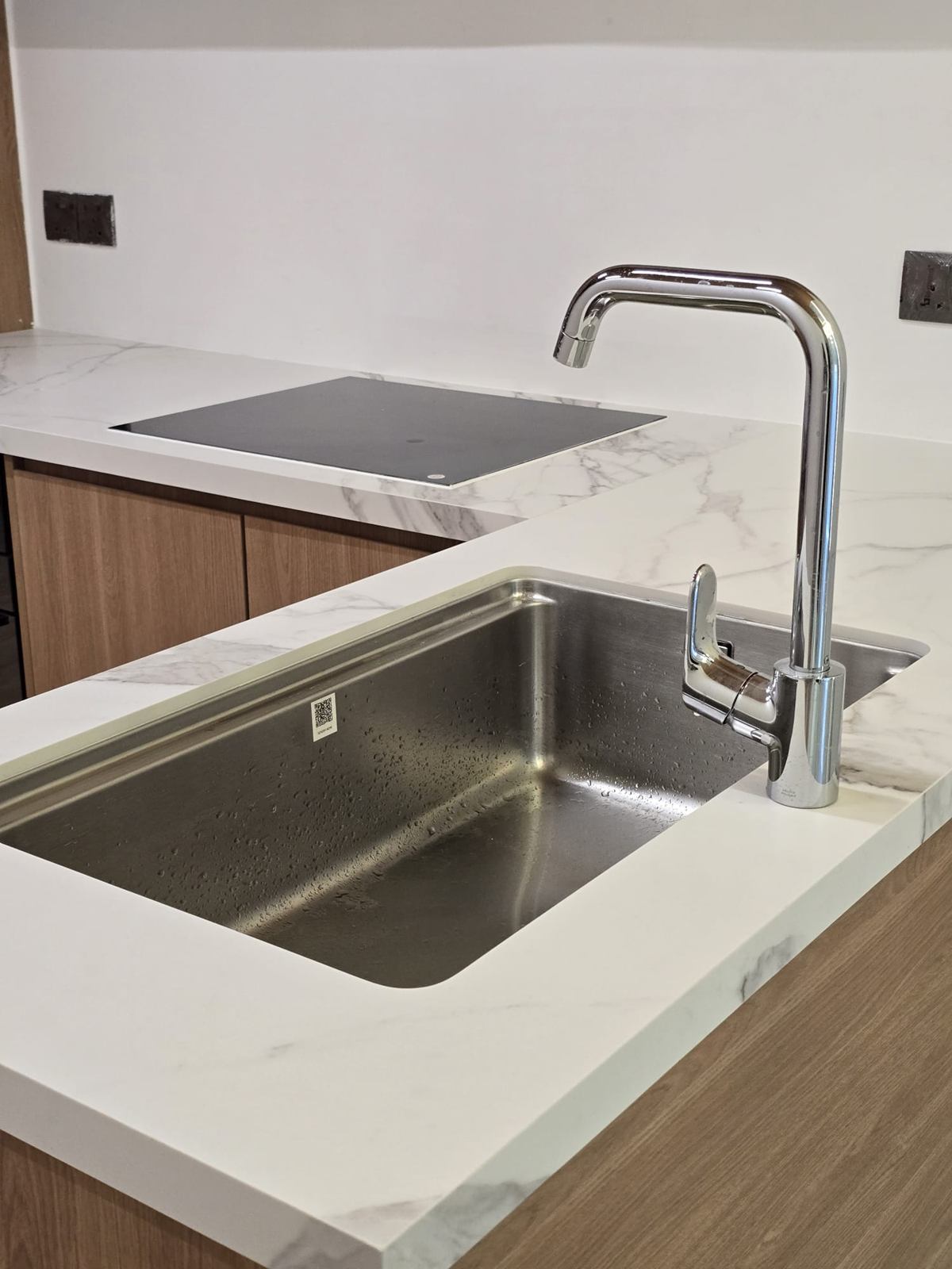 A stainless undermount sink and chrome tap in a white marble-look worktop.